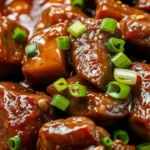 A close-up of a traditional Beef Pares dish featuring tender beef chunks in a glossy soy-based sauce, served with garlic fried rice and a bowl of clear beef soup.