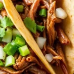 Beef birria tacos filled with tender shredded beef, crispy golden tortillas, and garnished with fresh onions and cilantro, served with lime wedges and a bowl of consommé for dipping.