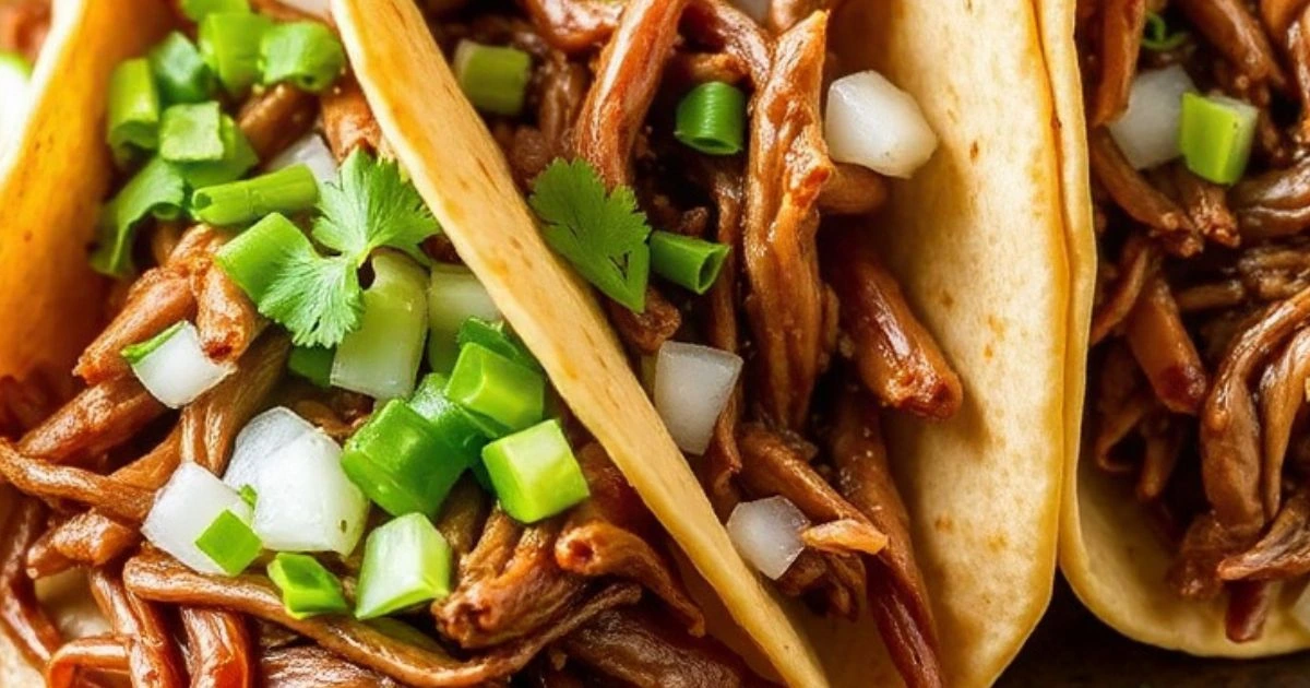 Beef birria tacos filled with tender shredded beef, crispy golden tortillas, and garnished with fresh onions and cilantro, served with lime wedges and a bowl of consommé for dipping.