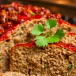 Sliced meatloaf with onion soup mix topped with glaze and garnished with herbs