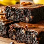 Fudgy banana brownies with chopped walnuts on a wooden board, featuring a rich chocolate texture and a glossy top.