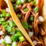 Close-up of beef birria tacos with juicy shredded beef, diced onions, fresh cilantro, and chopped green chilies in warm corn tortillas.