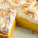 Close-up view of a sliced Lemon Meringue Pie showing thick lemon filling, golden toasted meringue peaks, and a buttery crust.