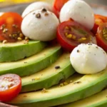 Avocado Caprese Salad with fresh mozzarella balls, sliced avocado, and cherry tomatoes seasoned with cracked pepper.