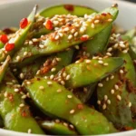 Spicy edamame pods tossed with garlic chili sauce and sprinkled with sesame seeds in a white bowl